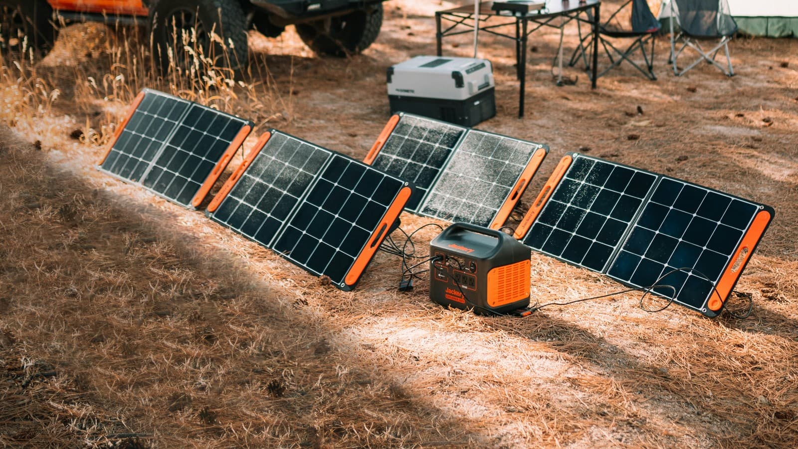 Portable folding solar panels and a black-and-orange power station connected by cables at a wooded campsite.
