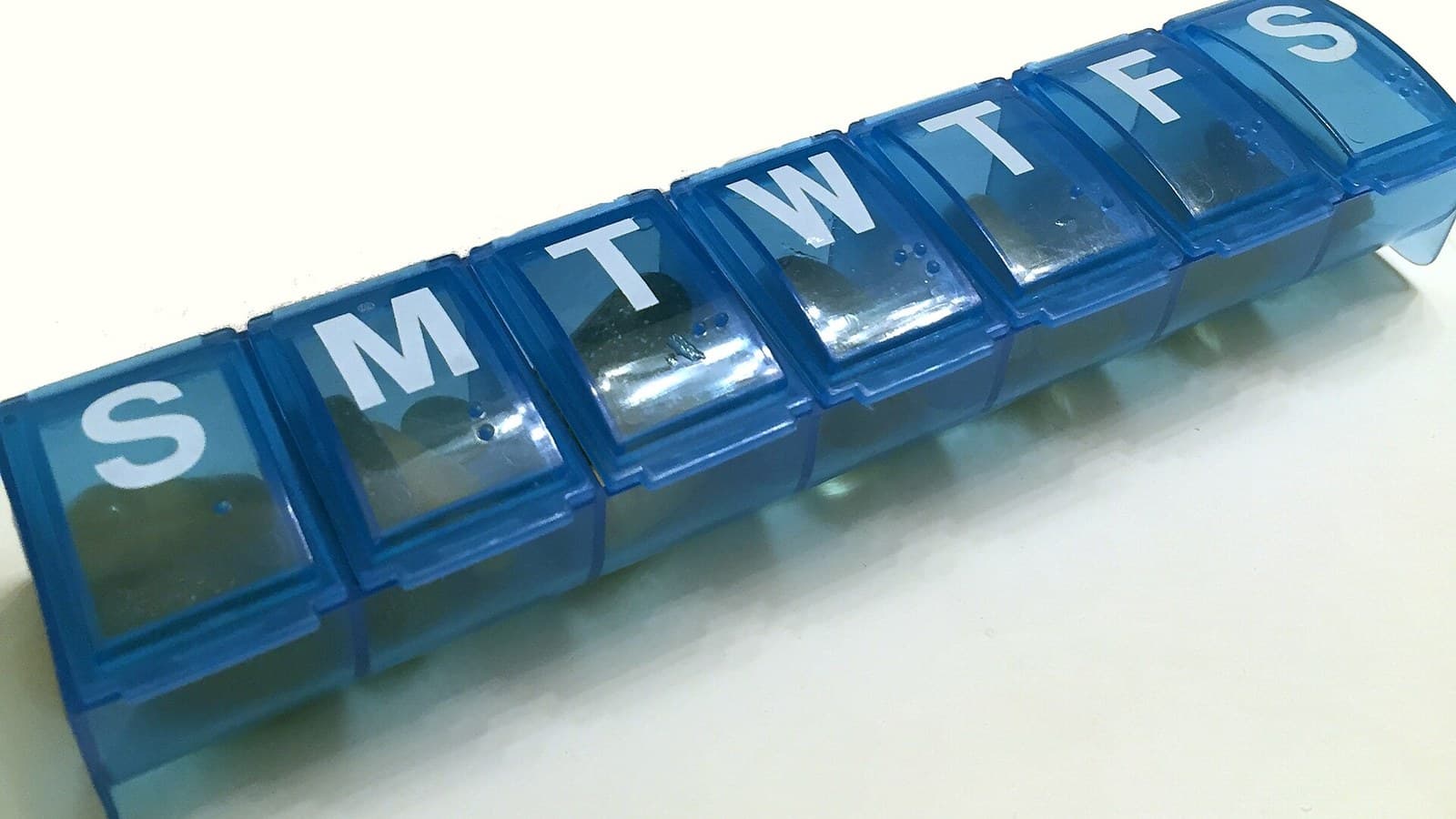 A blue weekly pill organizer with labeled daily compartments.