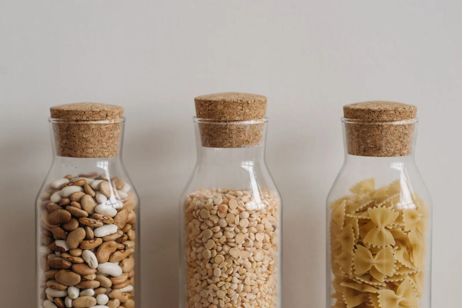 Stock photograph of three cork-lidded glass containers holding beans, split pulses and pasta.